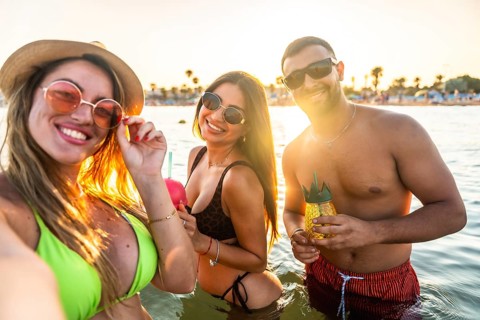 Young men and women having fun in the sea taking a selfie at sunset, enjoying refreshing cocktails