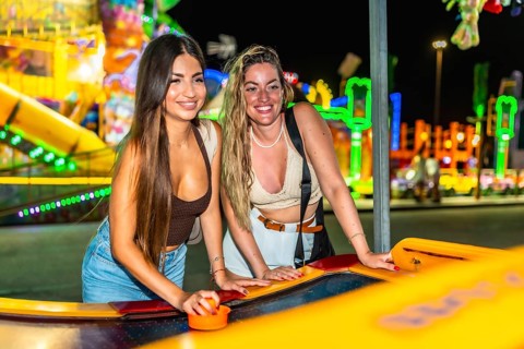Two friends enjoying a game of air hockey at a brightly lit amusement park, adding excitement to