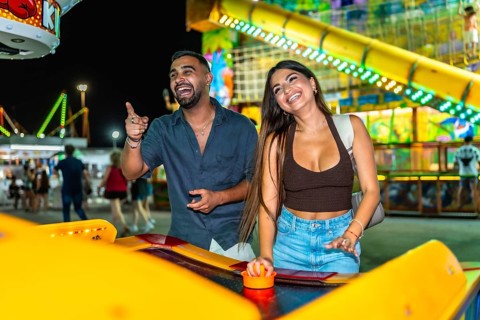 Young couple laughing and playing air hockey at an amusement park at night, enjoying their time
