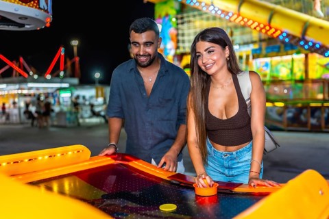 Happy young couple enjoying a lively night out, playing air hockey together at a colorful amusement