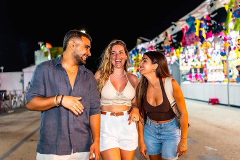 Group of three young friends laughing and walking together in an amusement park, enjoying the