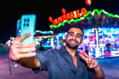 Happy young man smiling and taking a selfie while gesturing a peace sign, surrounded by vibrant