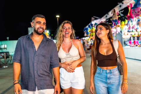 Three friends are enjoying their time together, strolling through a vibrant amusement park at night