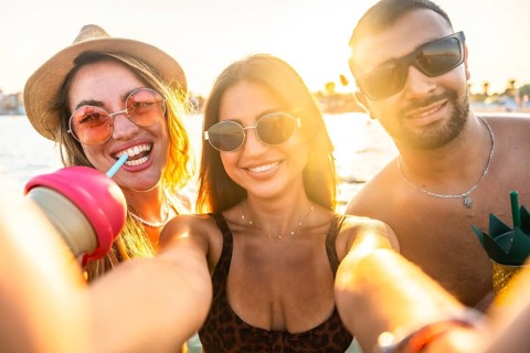 Group of cheerful multi ethnic friends taking selfie at beach party, enjoying refreshing drinks
