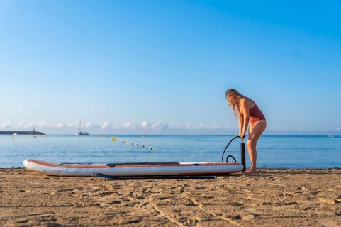 Woman inflating her paddle board on a beautiful sandy beach, preparing for a summer adventure on