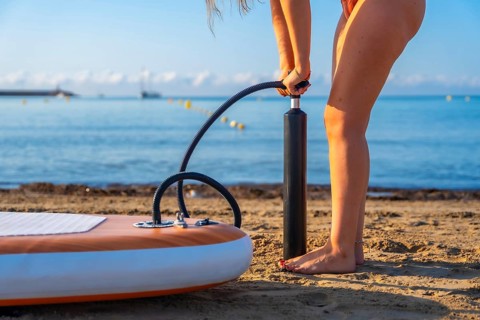 Woman inflating a paddleboard on a sandy beach, preparing for a summer paddle surfing session. Calm