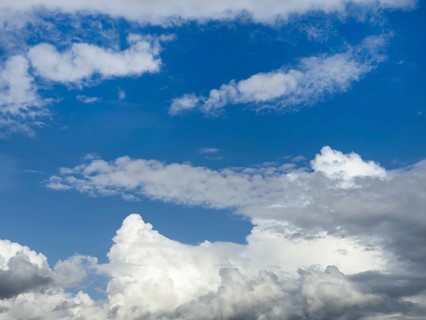 Below white cumulus clouds, centre above stratocumulus above altostratus in front of blue sky,