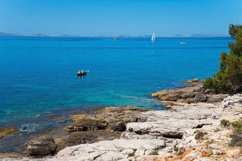Rocky coast with clear water and sailing boat under blue sky, Slanica, town of Murter, island of
