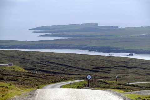 Coastal road winds through rolling countryside with views of the sea and distant islands, Eshaness,