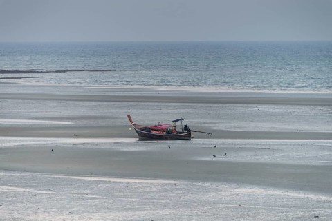 Before sunrise, a lonely longtail boat lies at low tide in the harbour at Sivalai Beach, Koh Mook