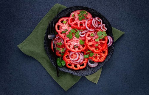 Freshly sliced tomatoes and red onions, garnished with herbs, on a black plate, summer salad, no