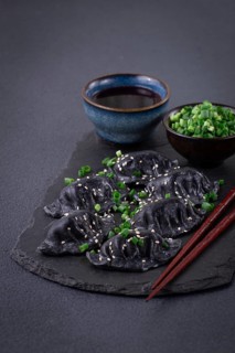 Japanese gyoza dumplings, made of black dough, black gyoza, with green onions and sauce, on a