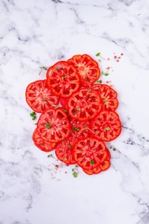 Freshly sliced ripe tomatoes arranged on a marble surface with microgreens and sea salt for a
