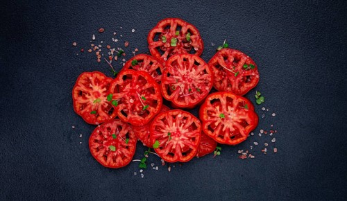 Freshly sliced ripe tomatoes arranged on a textured dark surface with herbs and salt scattered