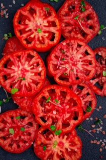 Freshly sliced ripe tomatoes arranged on a textured dark surface with herbs and salt scattered