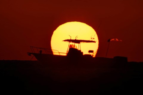The sun rises behind a boat on the Costa Rei, a coastal stretch of the Italian Mediterranean island