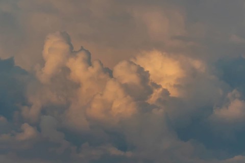 Fluffy clouds fill the sky, tinted by soft oranges and yellows as the sun is setting. The tranquil