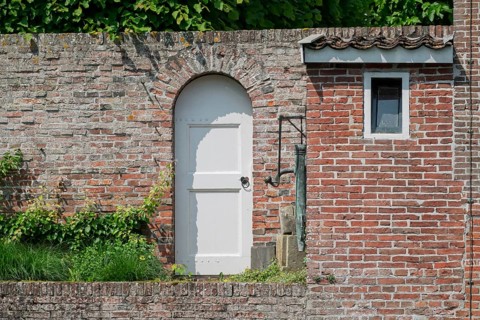White arched door in an old brick wall with green ivy above, Borg Verhildersum, Leens, province of