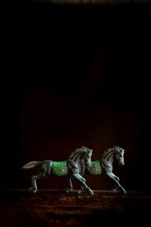 Two intricately designed horse figurines are positioned side by side, appearing to run forward. The