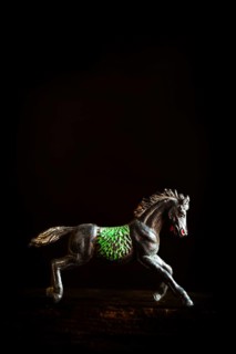 A black horse figurine is captured in mid-gallop, showcasing detailed green patterns on its side.