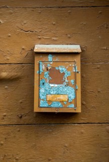 A weathered mailbox hangs on a rustic wooden wall, showcasing chipped paint in blue and brown tones
