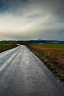 A winding road stretches through green fields under a cloudy sky, showcasing the beauty of the