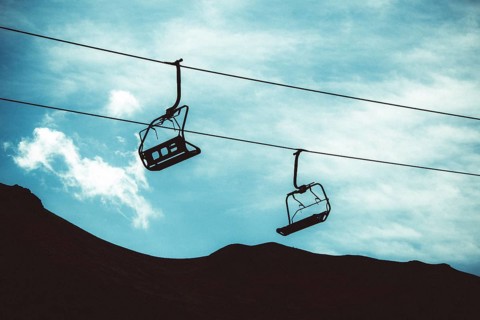 Two empty ski lifts hang from cables, silhouetted against a backdrop of a dark mountain and cloudy