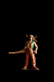 Vintage Native American Indian toy figure stands boldly in a dark setting, wielding a long weapon