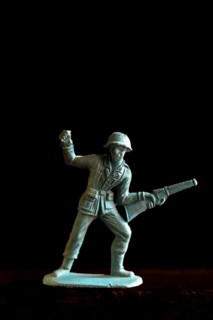 A plastic soldier figurine stands confidently with a rifle and raised fist, captured in warm