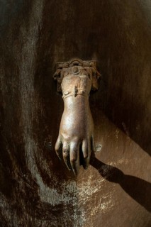 A decorative hand-shaped door knocker is firmly mounted on a weathered wooden door showcasing rich