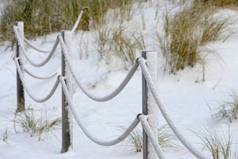 Winter day, onset of winter, demarcation poles with ropes in the snow-covered dune landscape of