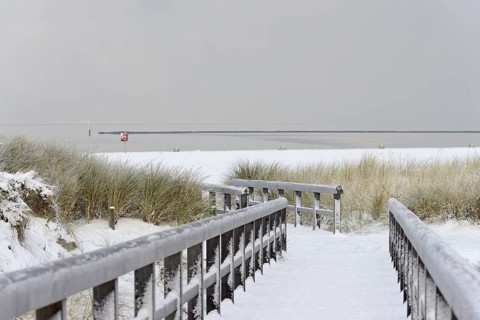 Winter day, onset of winter, wooden plank path leads through the snow-covered dune landscape to the