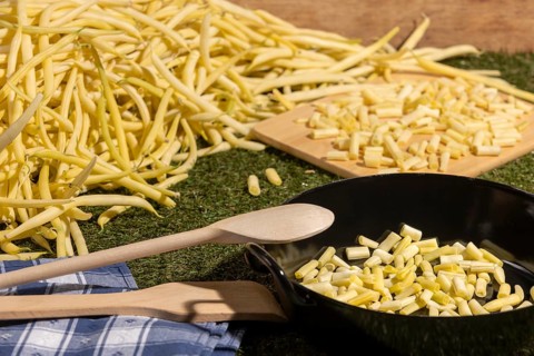 Pan with sliced yellow runner beans and a wooden spoon, beans in the background