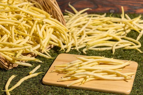 A basket of yellow beans, some on a board on a green background