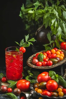 Rustic still life with tomatoes, tomato juice and herbs in a dark setting