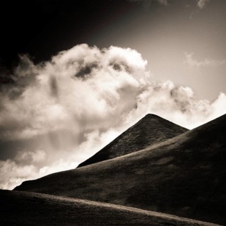 A striking view of a mountain peak stands tall against a backdrop of swirling clouds. Sancy Massif,