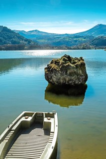 Lake chambon reflects the stunning blue sky and surrounding mountains. A small boat rests at the