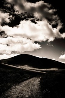 A winding path leads towards a dark mountain silhouette against a dramatic sky filled with
