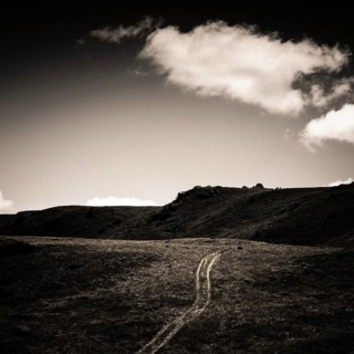 A dirt trail meanders through a rugged terrain with rolling hills and dramatic skies. Auvergne