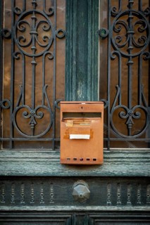 A rusty mailbox is affixed to a beautifully crafted wrought iron door. The intricate ironwork