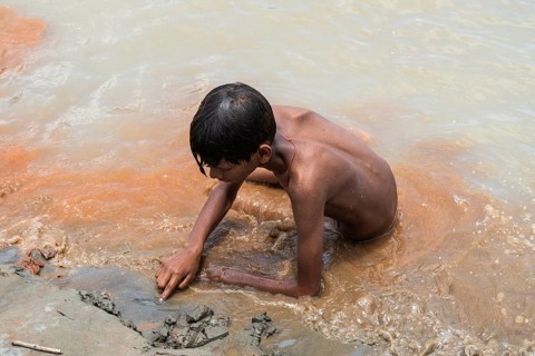 A boy sits in the bank of Brahmaputra River as he bathe to seek relief from the intense summer heat