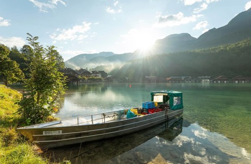 Beautiful morning at the Königssee in Schönau with a boat and boathouses in the background. Sunrise