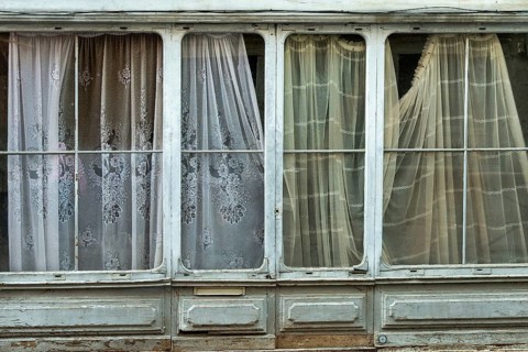 Light streams gently through patterned curtains hanging in a historic building, creating an