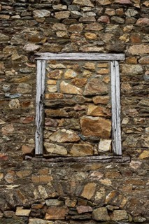 This rustic wall features a stone layout with various textures, framed by an aged wooden window.
