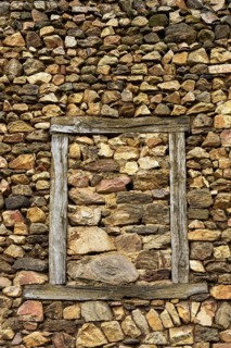 A wall constructed of unevenly arranged stones features a striking wooden frame that outlines an