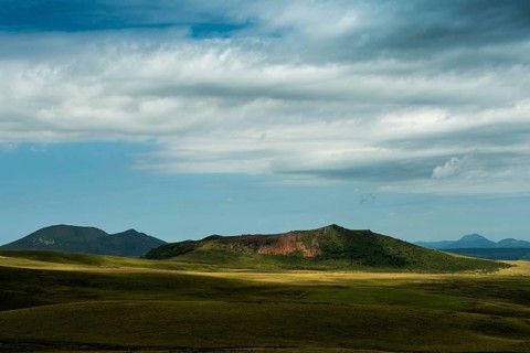 Mountains stretch across the landscape under a vast sky filled with dynamic clouds. Sancy Massif in