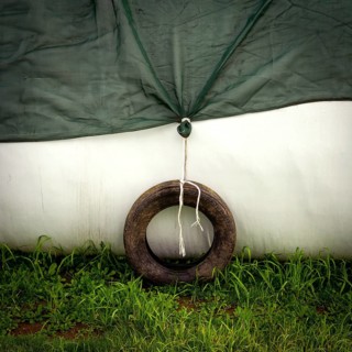 A weathered tire is tied to a green tarp, providing stability in a subtle, serene outdoor setting.