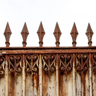 An old, weathered wrought iron fence features intricate scrollwork and pointed spikes atop its