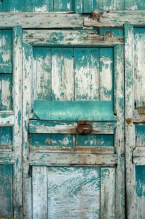 The weathered wooden door features peeling teal paint and rough textures, showcasing its rustic