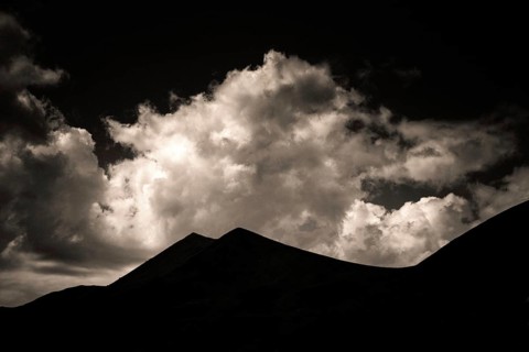 Majestic mountains form a dark outline against a backdrop of swirling clouds illuminated by